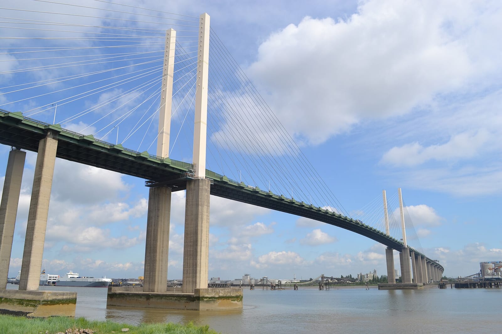 The Queen Elizabeth II Bridge seen from the riverbank below, its cables and piers rising over the Thames.